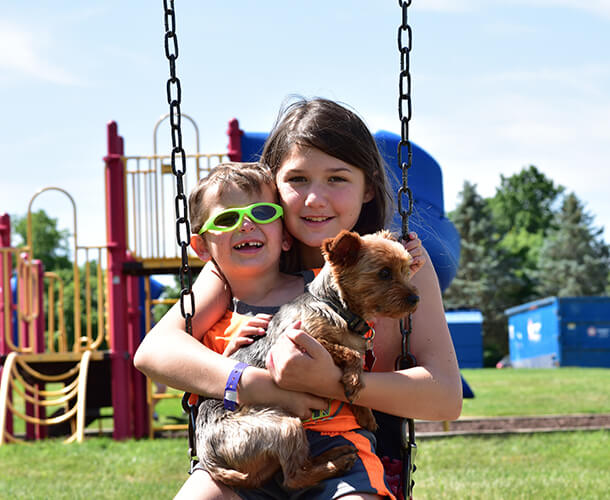two kids, a sister and brother sitting on a swing together holding their puppy - Find homes for sale in parks in Delaware